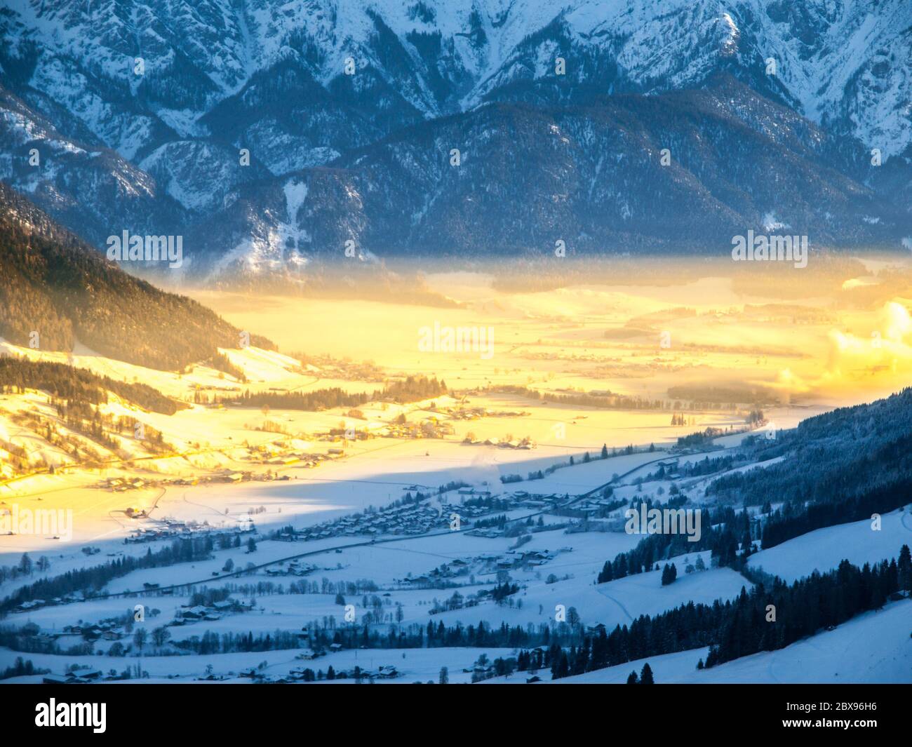 Morning in alpine valley. Winter haze illuminated by ray of rising sun, Leogang, Austria. Stock Photo