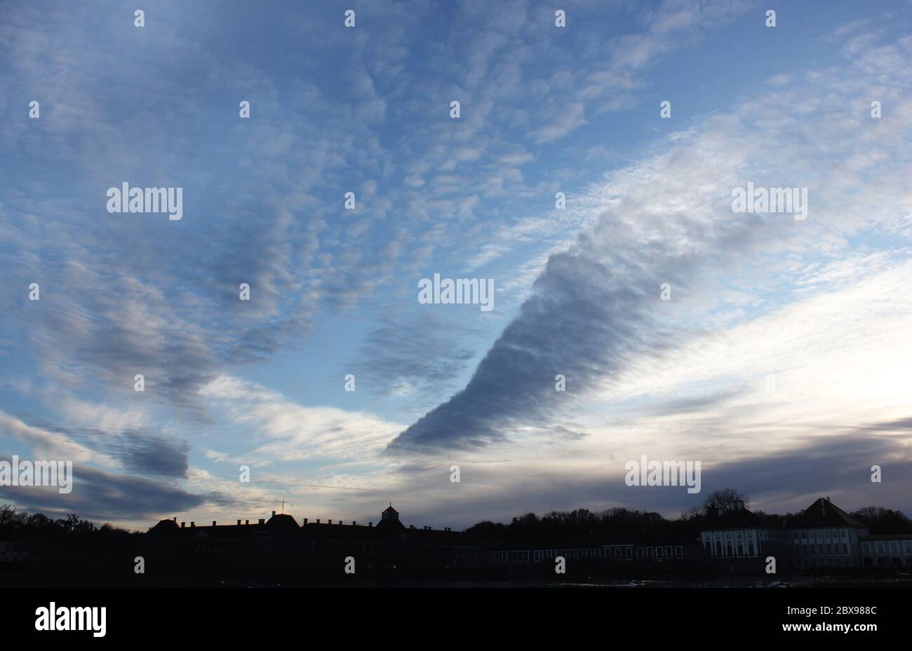 Dramatically sharp wedge shaped cloud formation over a palace silhouette at sunset. Unique arrow or triangle cloud structure. Dynamic sky backdrop. Stock Photo