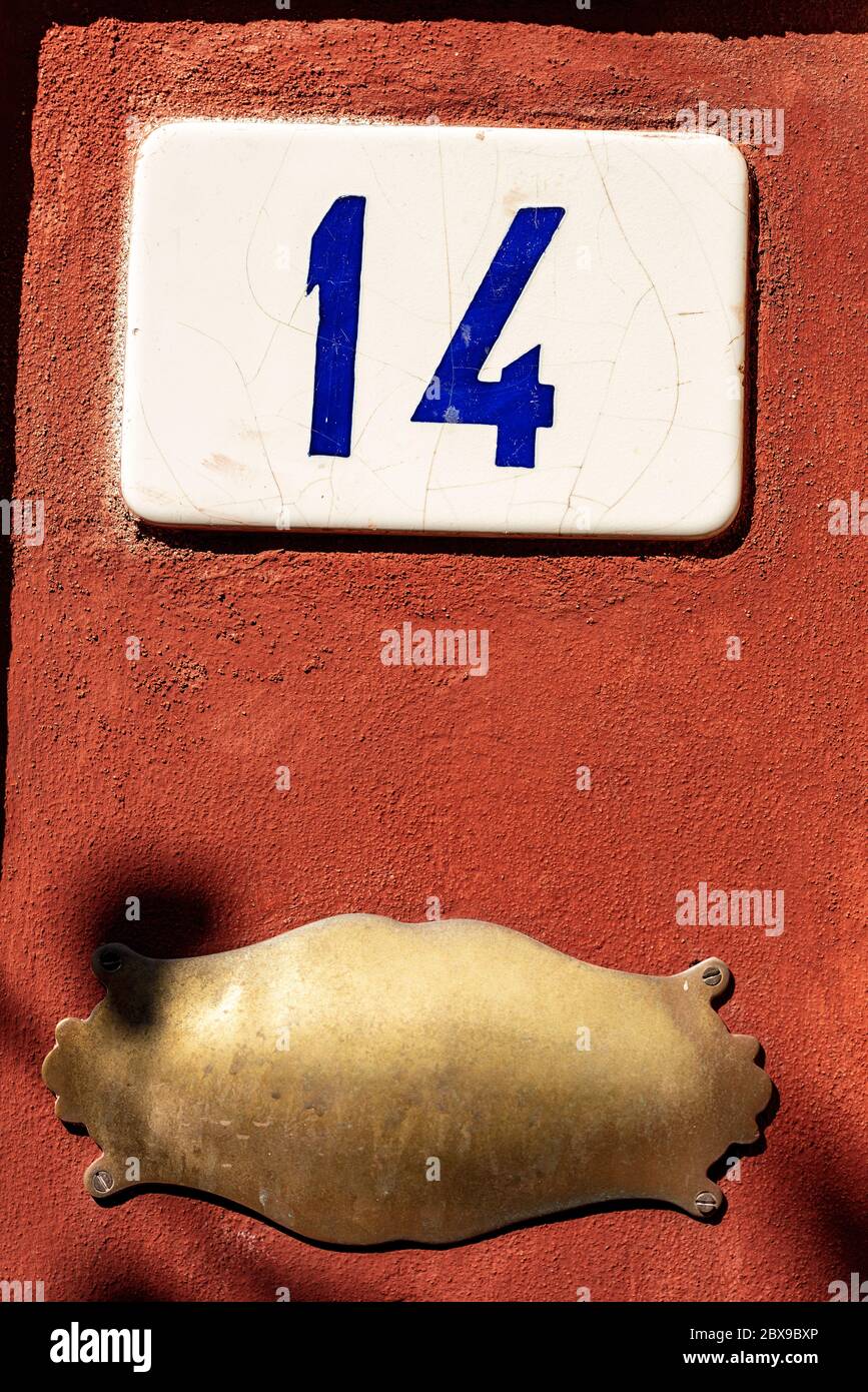 Old house number fourteen and an empty brass plaque with copy space on the red wall, Liguria, Italy, Europe Stock Photo