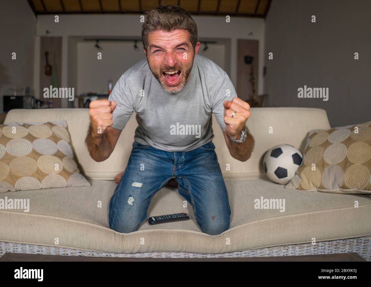 30s or 40s football fan man watching soccer game celebrating his team scoring goal crazy happy screaming cheering his team sitting at home living room Stock Photo