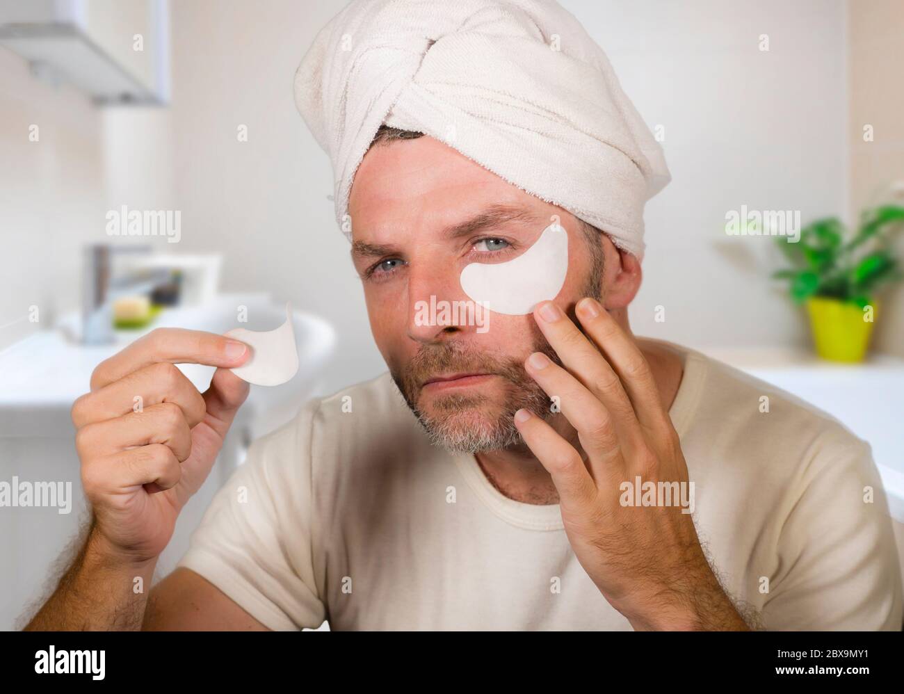 funny portrait of young happy and attractive camp gay man in bathroom  applying moisturizer eye patch facial product with head wrapped in towel  feeling Stock Photo - Alamy