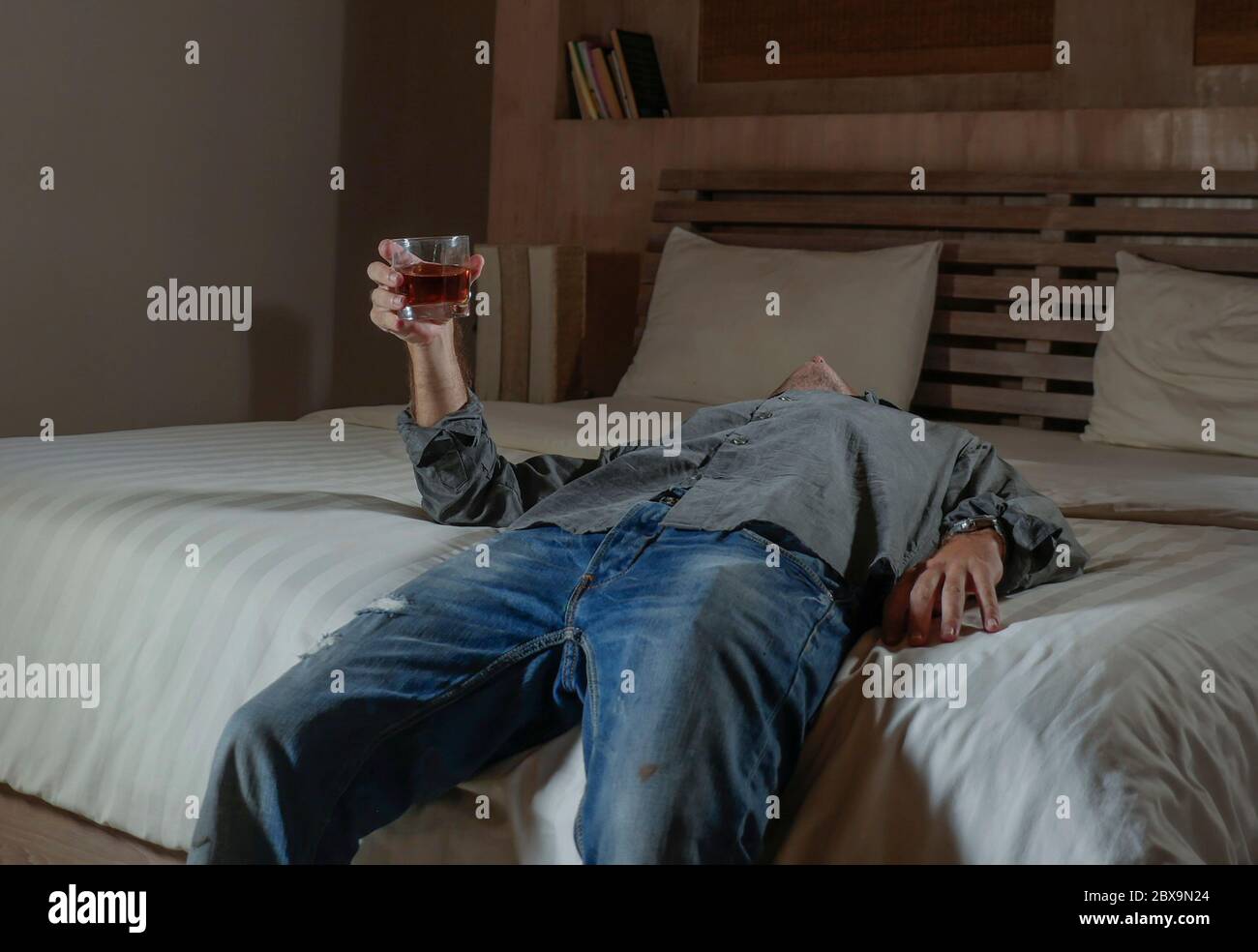 young messy and wasted drunk man drinking whiskey glass at home lying on bed hammered and dizzy