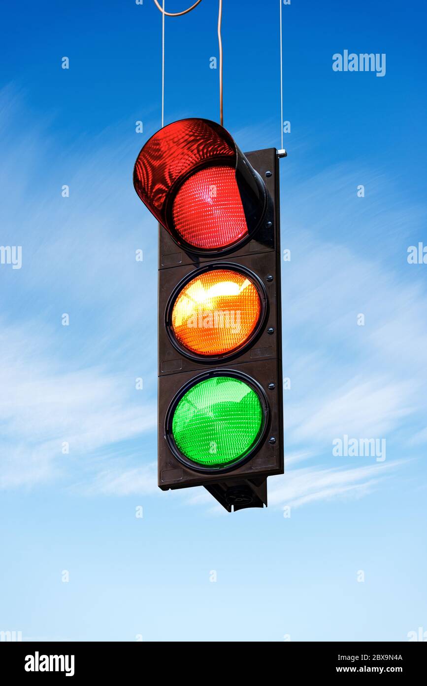 Traffic light on a blue sky with clouds, with all three lights on, green, orange and red. Stock Photo