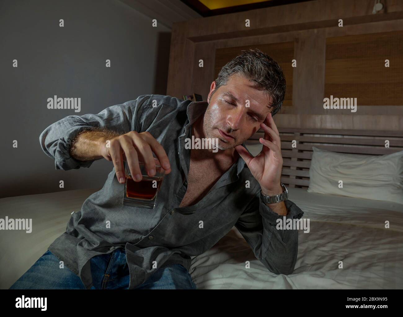 young messy and wasted drunk man drinking whiskey glass at home sitting