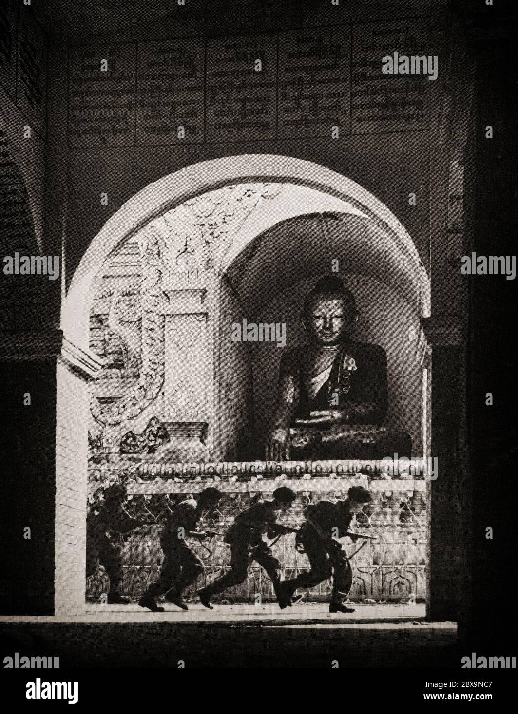 British and Indian soldiers creep passed a Buddha on Pagoda Hill as they charge an enemy position in Mandalay, during Operation Dracula, a World War II-airborne and amphibious attack on Rangoon by British, American and Indian forces during the Burma Campaign, launched during April and May 1945. Stock Photo