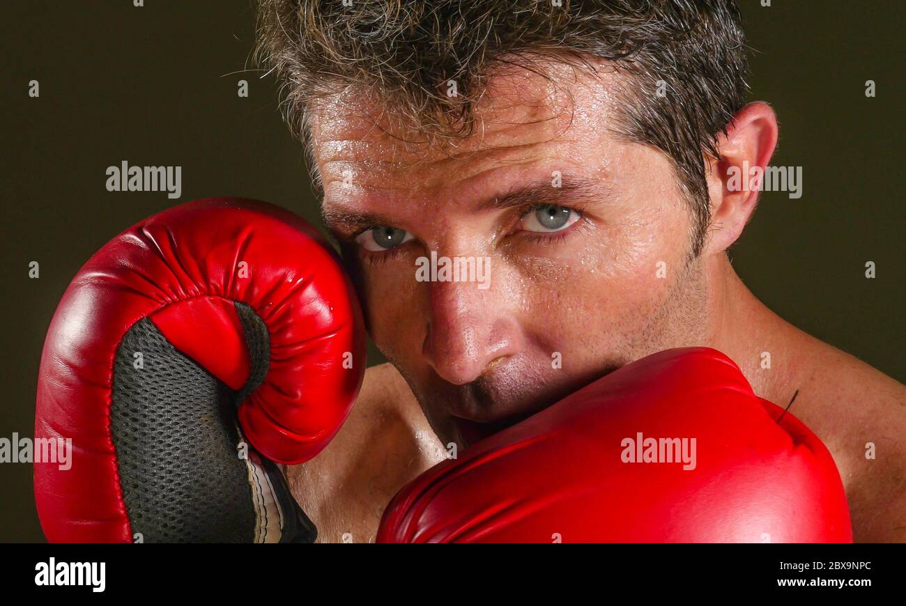 close up face portrait of young attractive and fierce looking man in boxing gloves posing in defense boxer stance isolated on dark background in sport Stock Photo