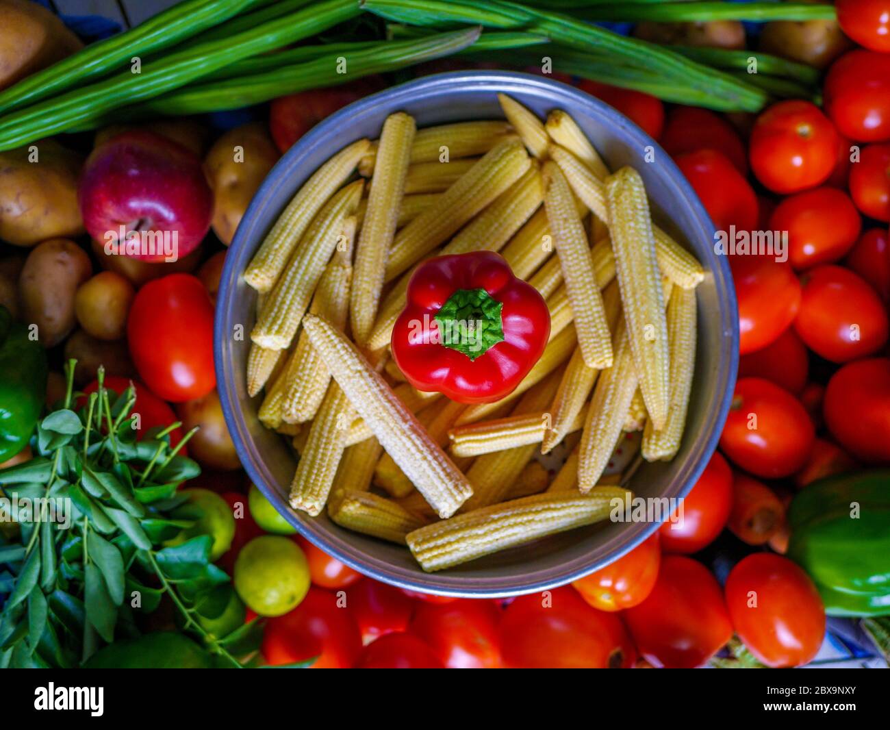 Red Capsicum and Baby corns arranged in a basket with tomatoes and green veggies in background Stock Photo