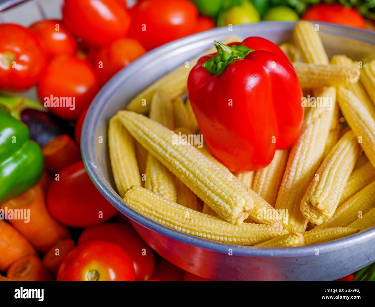 Red Capsicum and Baby corns arranged in a basket with tomatoes and green veggies in background Stock Photo