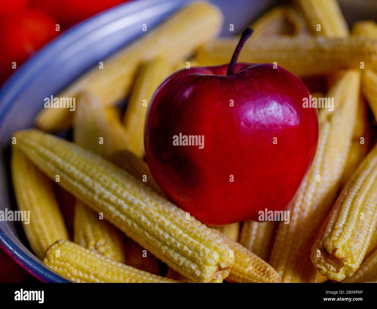 Fresh Apple and Baby corns arranged in a basket with tomatoes and green veggies in background Stock Photo