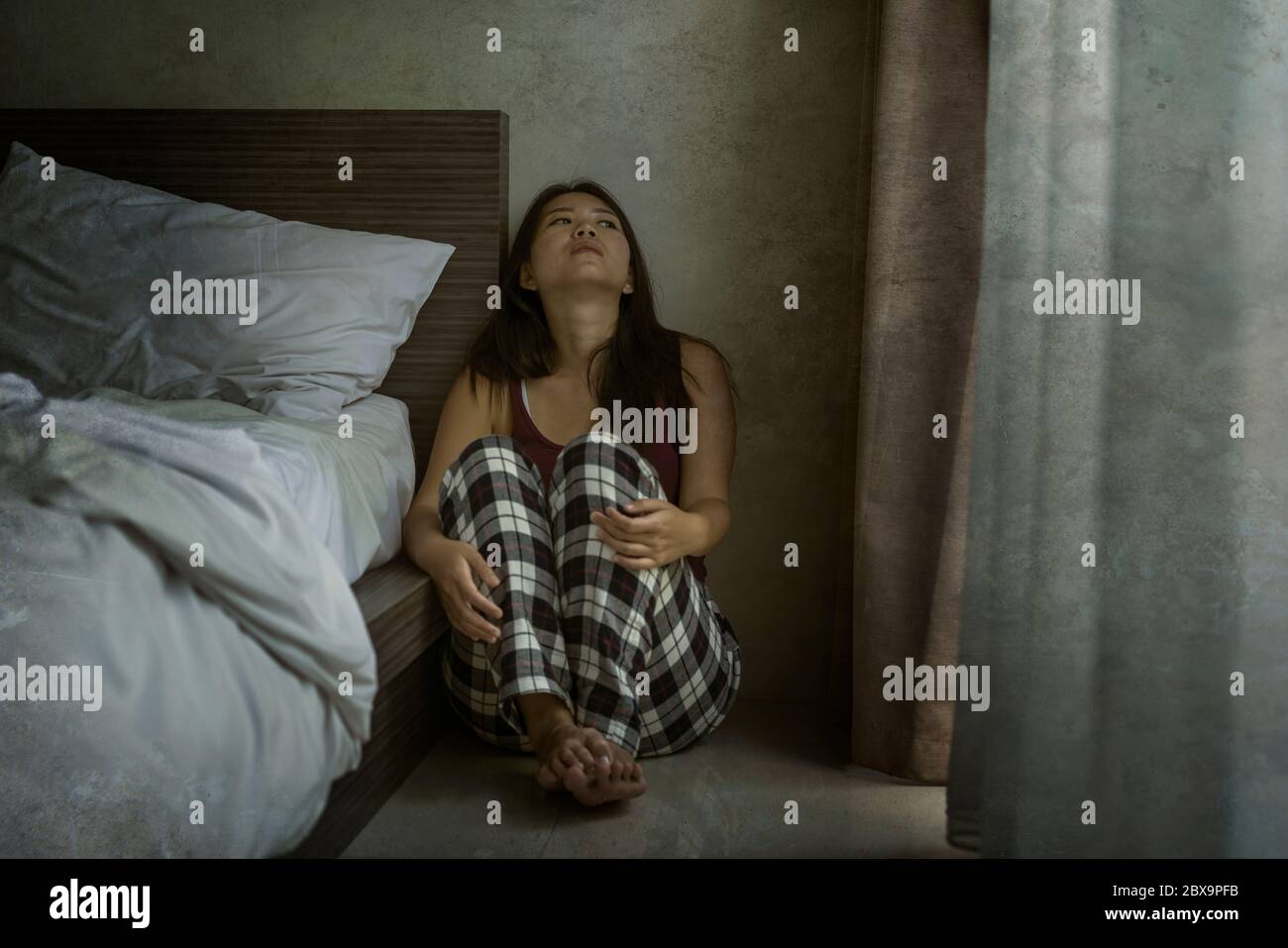 dramatic dark portrait of young attractive depressed and sad Asian Chinese woman on bedroom floor feeling worried and scared suffering depression prob Stock Photo