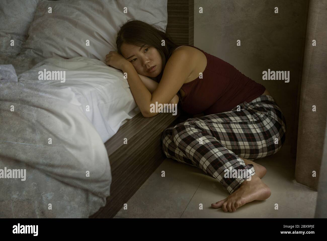 dramatic dark portrait of young attractive depressed and sad Asian Chinese woman on bedroom floor feeling worried and scared suffering depression prob Stock Photo