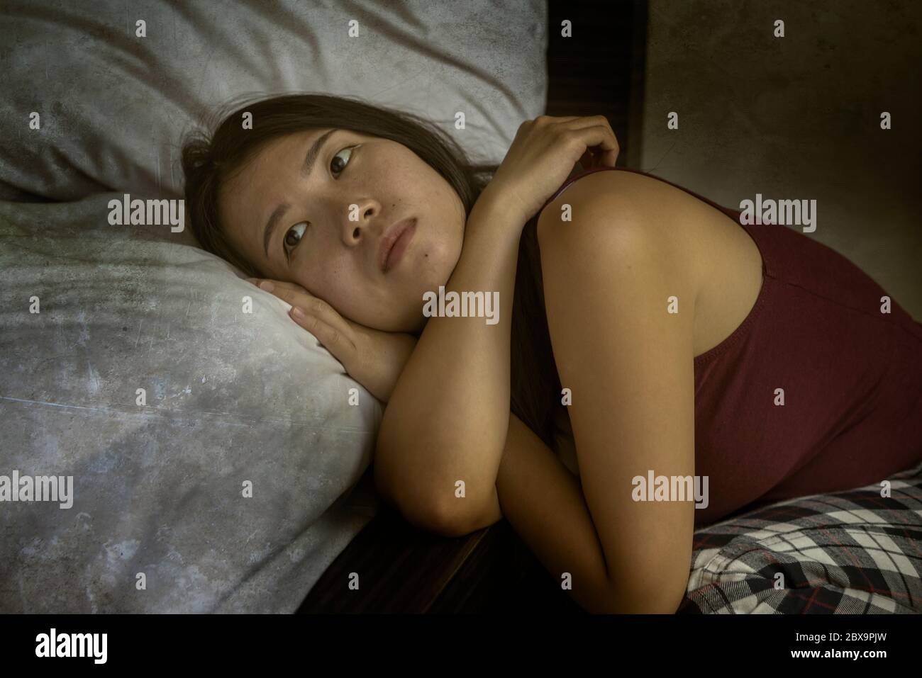 dramatic dark portrait of young attractive depressed and sad Asian Chinese woman on bedroom floor feeling worried and scared suffering depression prob Stock Photo