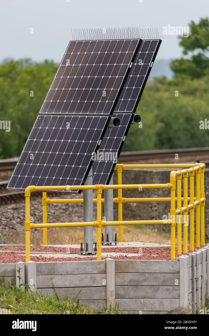 Solar energy panels with bird deterrent spikes on the top, mounted alongside railway tracks and surrounded by yellow scaffolding rails Stock Photo