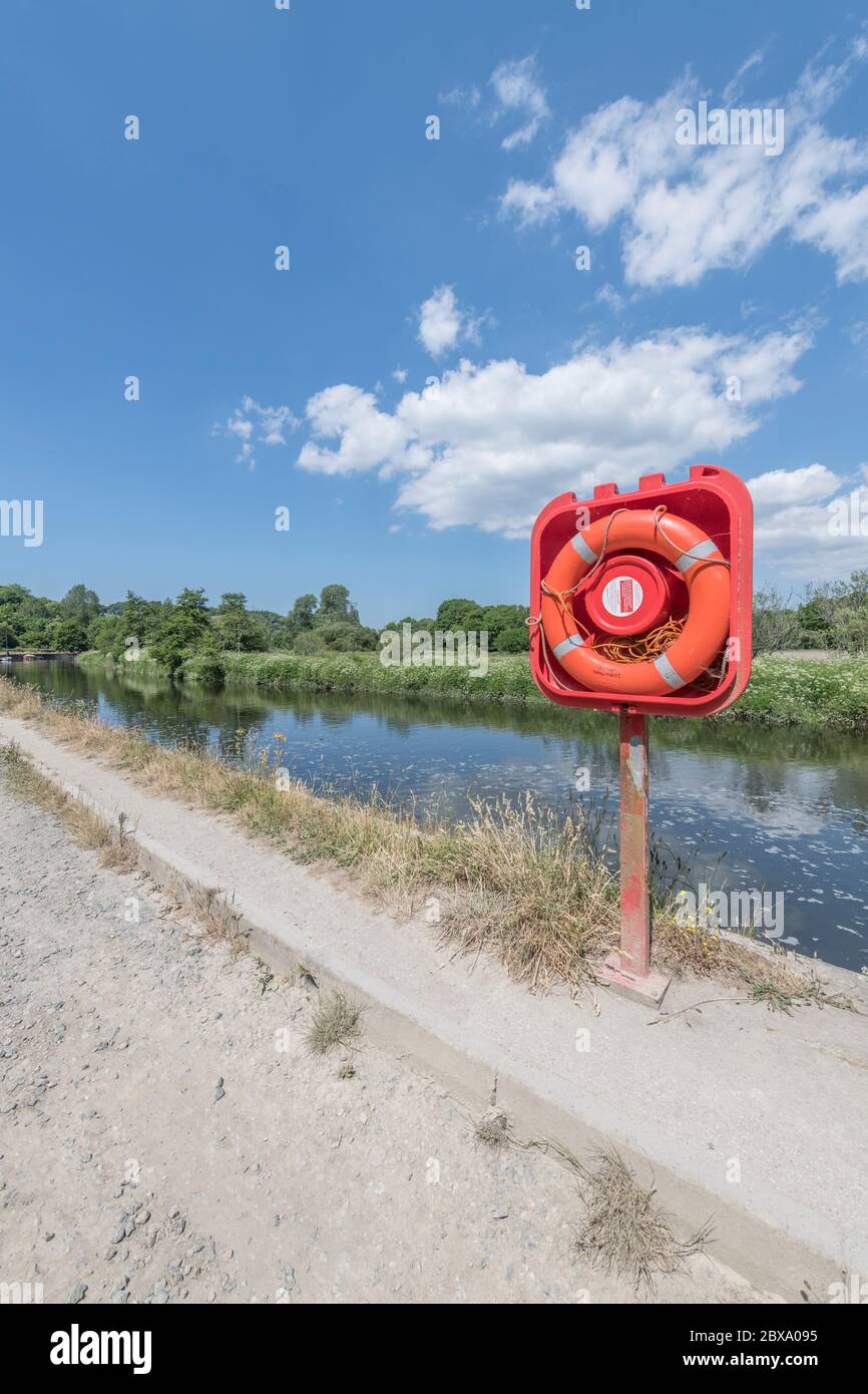 Sunlit bright orange-red lifebuoy ring in quayside housing on River Fowey at Lostwithiel. For safety, danger, staying afloat, possibly risk assessment Stock Photo