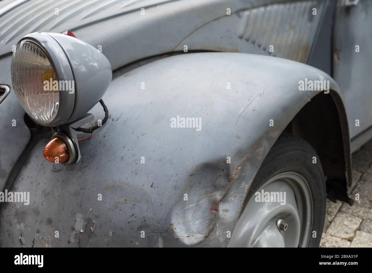 Front with headlight and a dent in the mudguard of an old run-down car (Citroen 2CV) in the village Raerd, The Netherlands Stock Photo