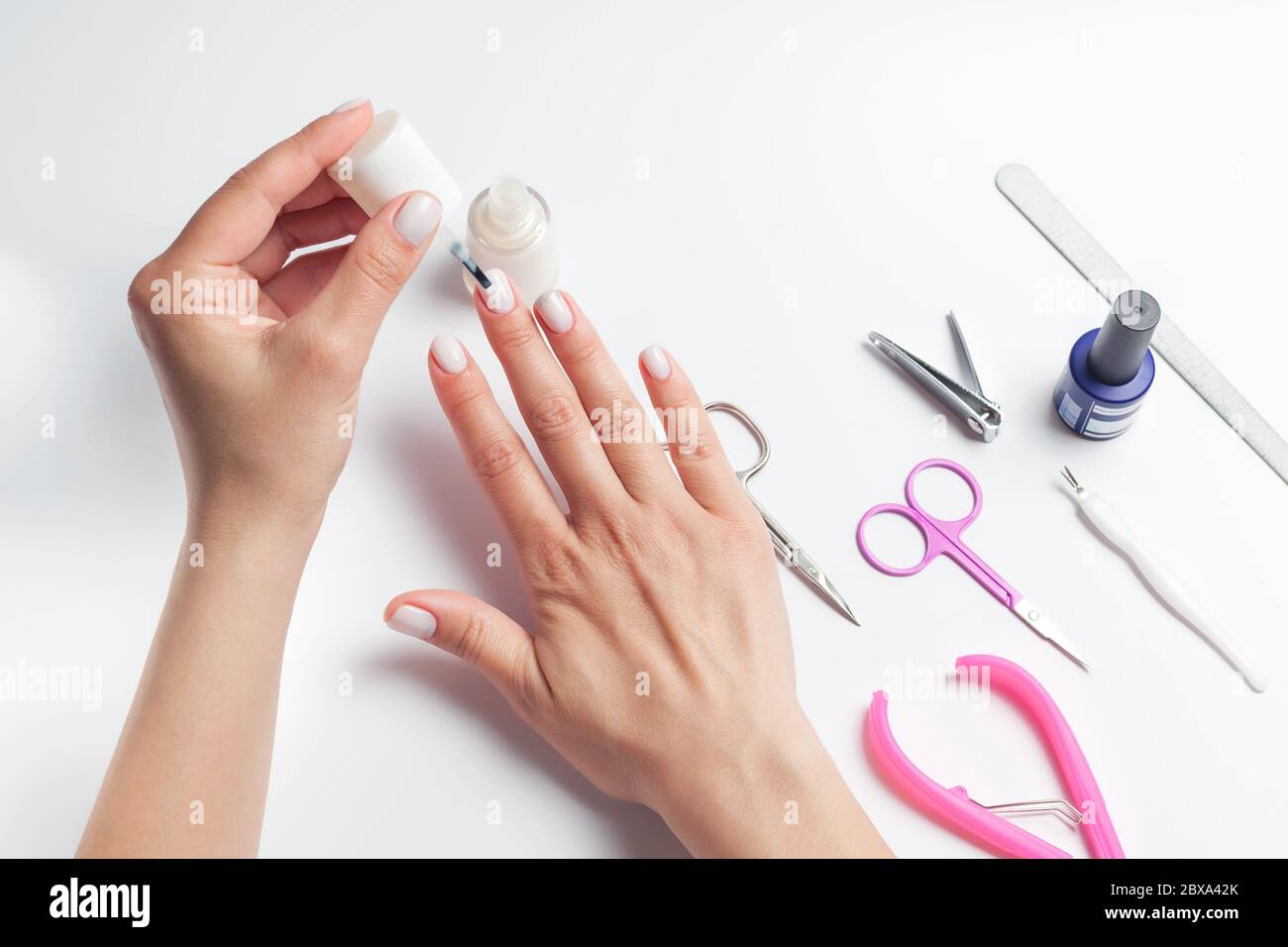 Female hands paint nails, next to lay down devices for nail care. The girl does a manicure. on white background. View from above. High quality photo Stock Photo