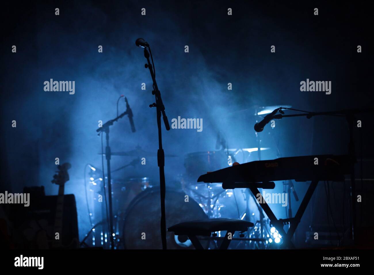 A stage set with instruments and microphones. The smoke and blue light that shows the silhouet of the mics gives a groovy vibe. A typical stage scene. Stock Photo