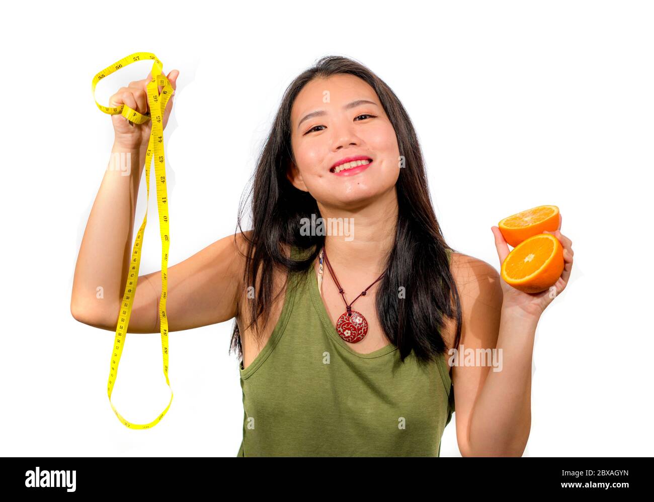 young happy and beautiful Asian Chinese woman holding orange fruit and ...
