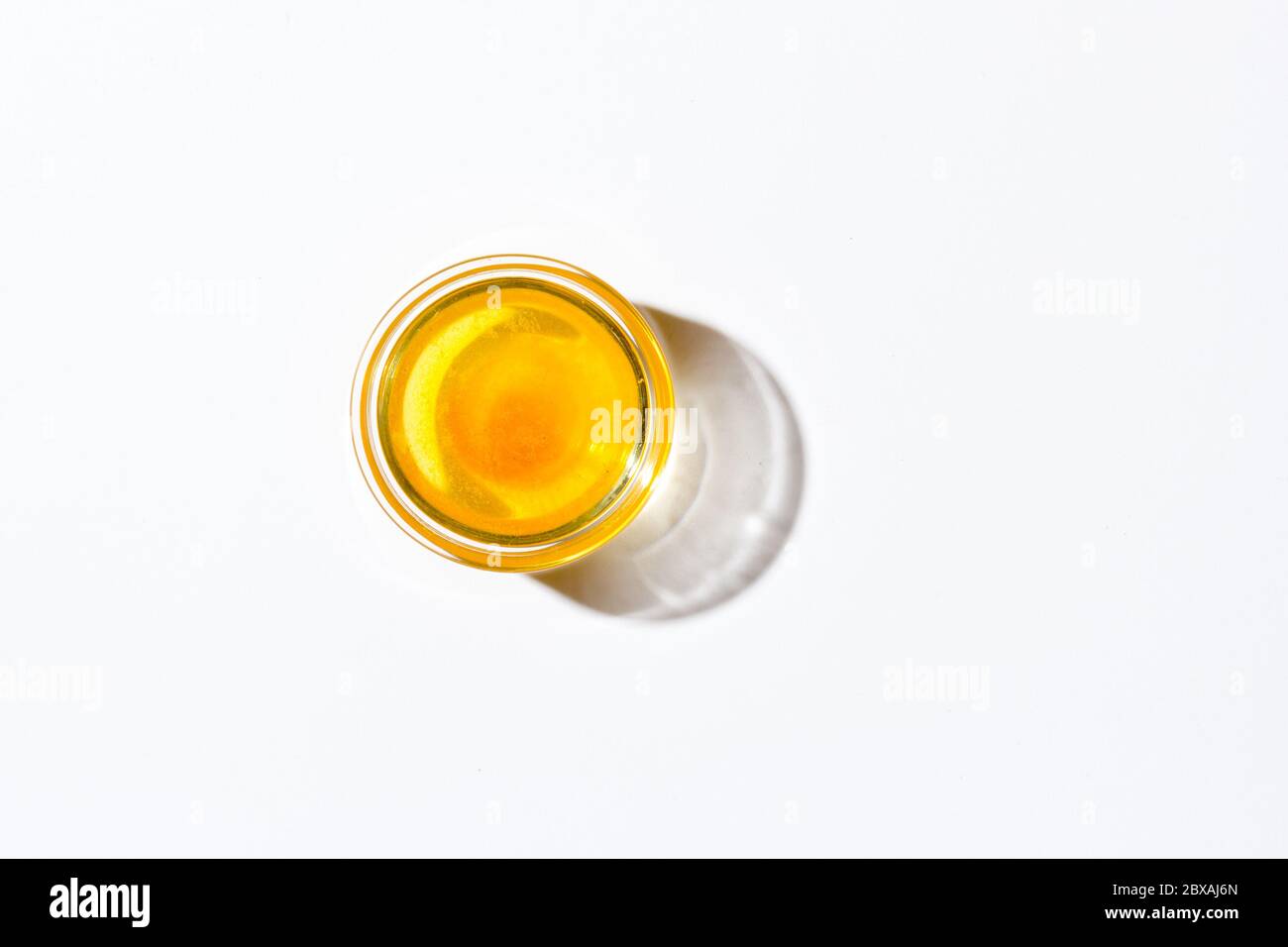 Honey in a small glass plate on a white background. Nearby lies a wooden spoon Stock Photo