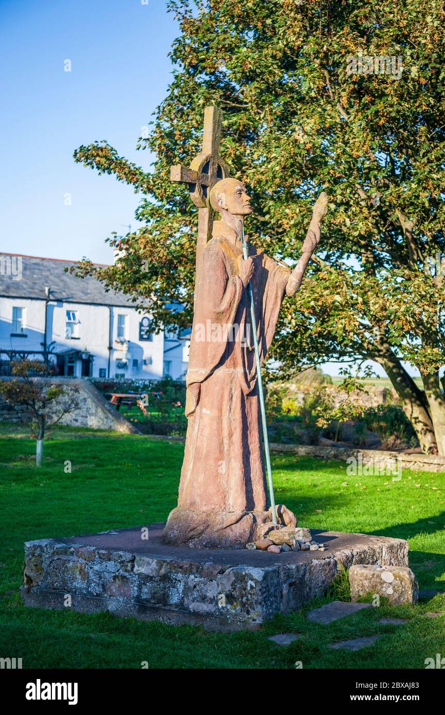 A modern statue of St Aidan of Lindisfarne next to the ruined Priory on