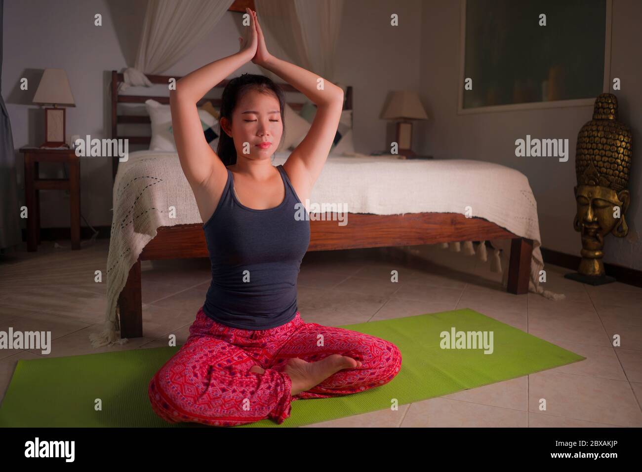 young happy and beautiful Asian Korean woman at home bedroom doing meditation workout on yoga mat relaxed and peaceful in wellness and healthy lifesty Stock Photo