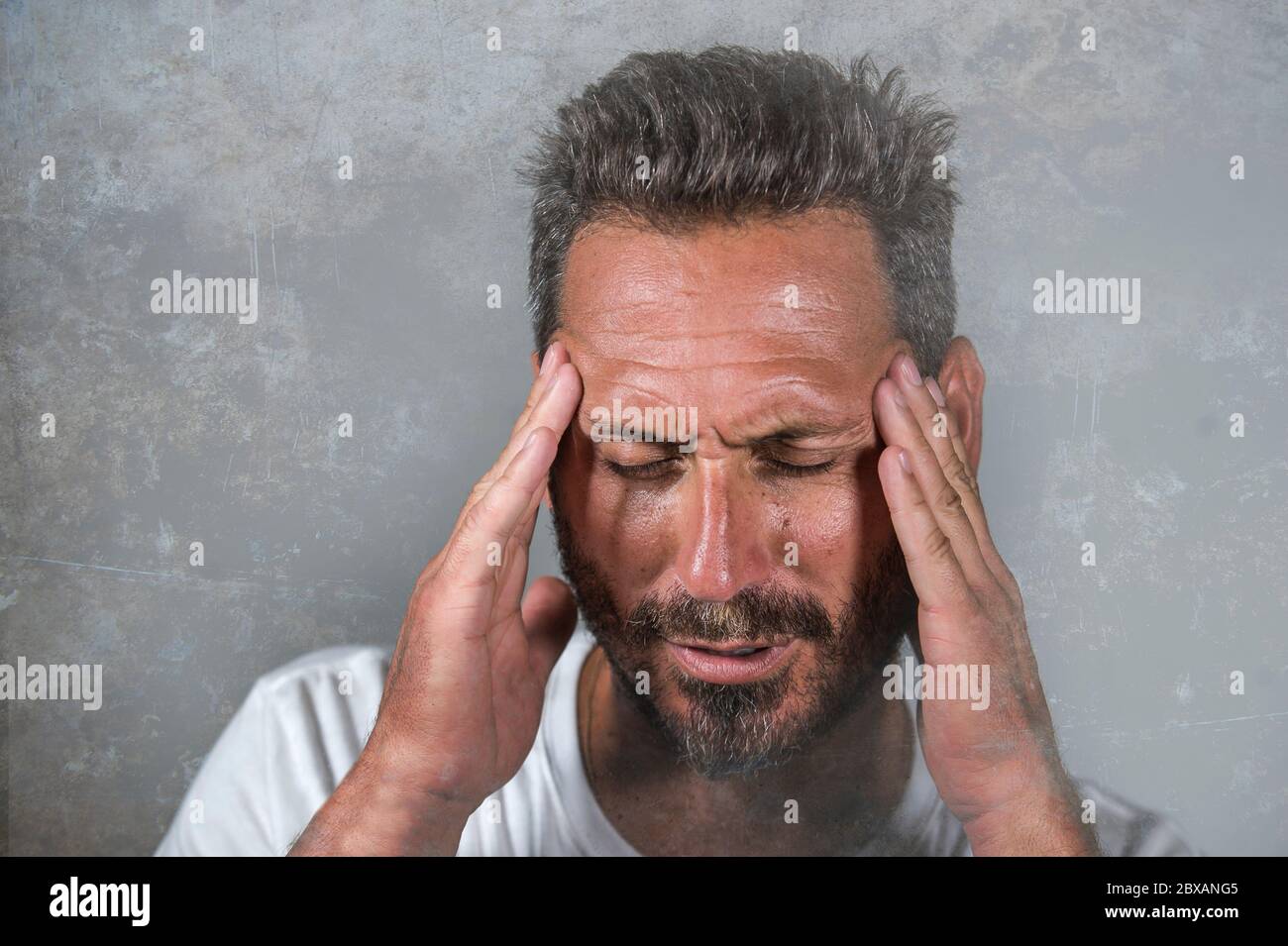 close up dramatic  portrait of young attractive anxious and depressed man in pain with hands on his head suffering headache and migraine and depressio Stock Photo