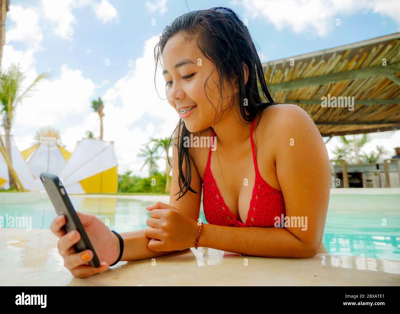 lifestyle portrait of young happy and beautiful Asian Indonesian teenager  girl in bikini taking selfie picture with mobile phone in beach hotel  swimmi Stock Photo - Alamy