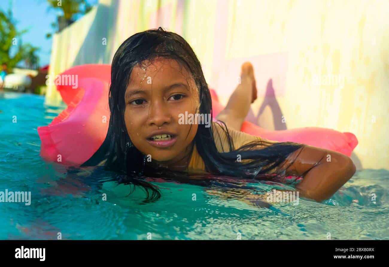 lifestyle outdoors portrait of young happy and cute female child having fun with inflatable airbed in holidays resort swimming pool smiling carefree a Stock Photo