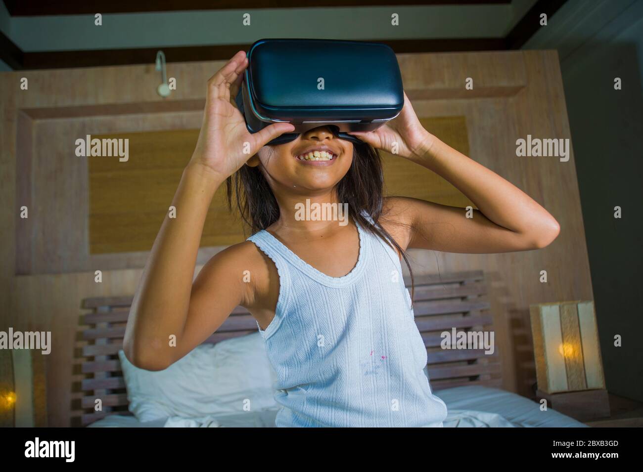 lifestyle portrait of young happy and excited female child wearing VR goggles device headset playing virtual reality simulation game enjoying an amazi Stock Photo