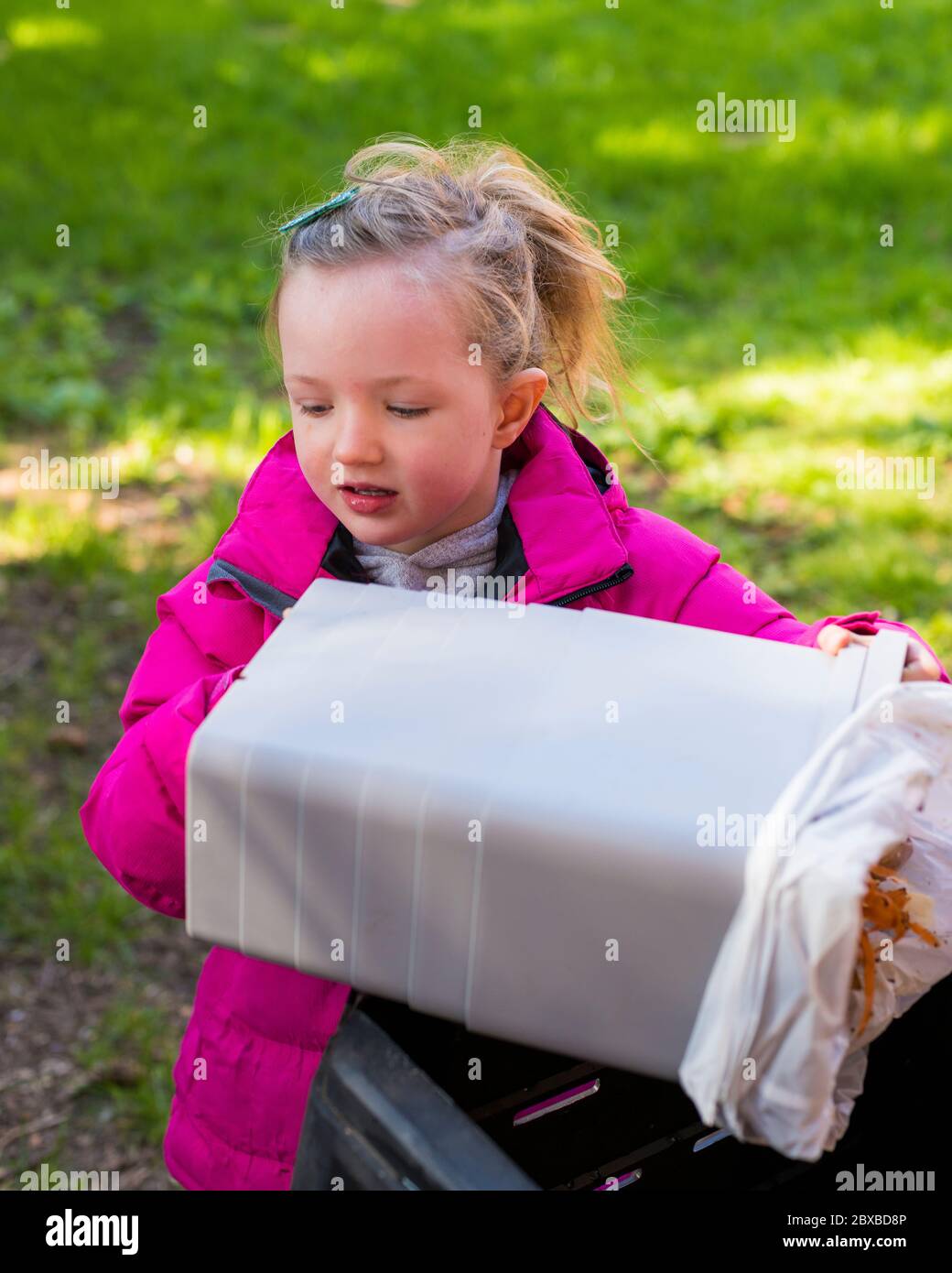 Pre-school girl emptying compost bin during lockdown, Girl wearing pink coat doing composting, Teaching pre-school girl about compost Stock Photo