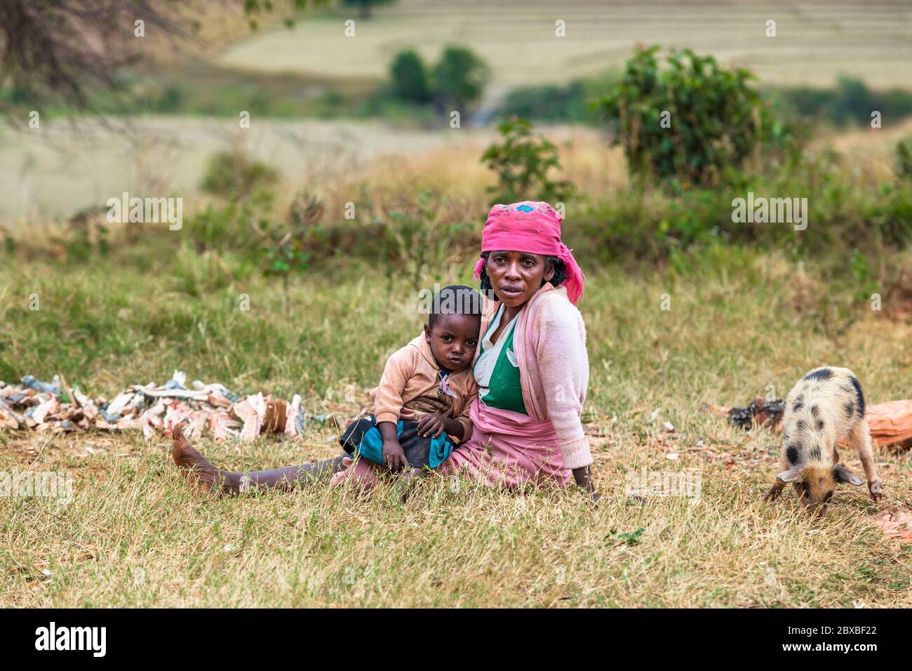 Tired african woman with child sitting on green field. Central Madagascar Stock Photo