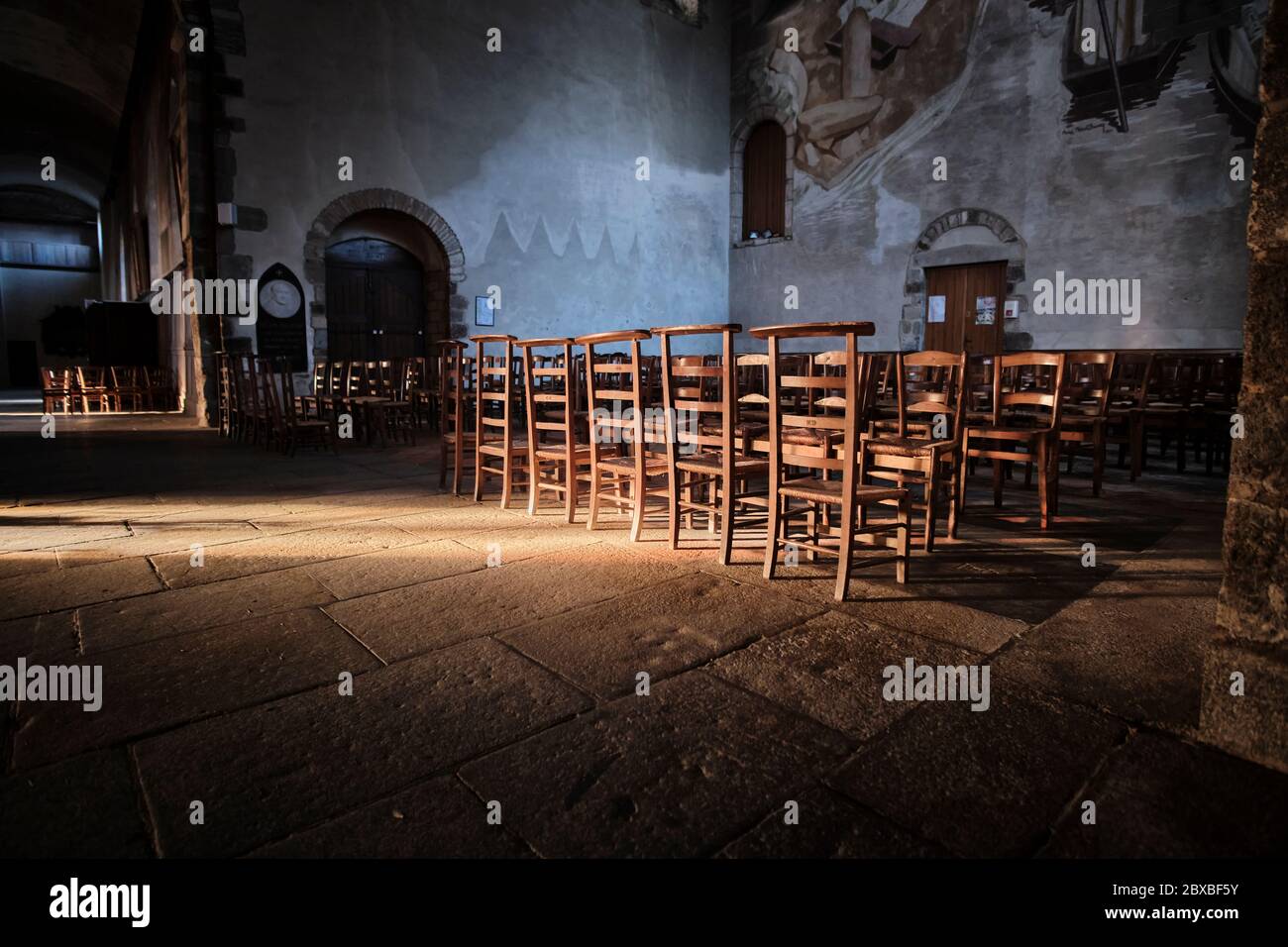 Wooden chairs and kneeling stools in the Transpet of the Church of St. Melaine with a stream of light illuminating the chairs and alcove Stock Photo