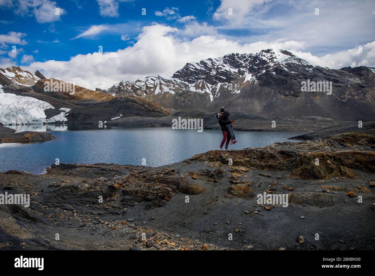 couple in a glacier, near a lake, mountains with snow in their peaks, clouds and blue sky Stock Photo