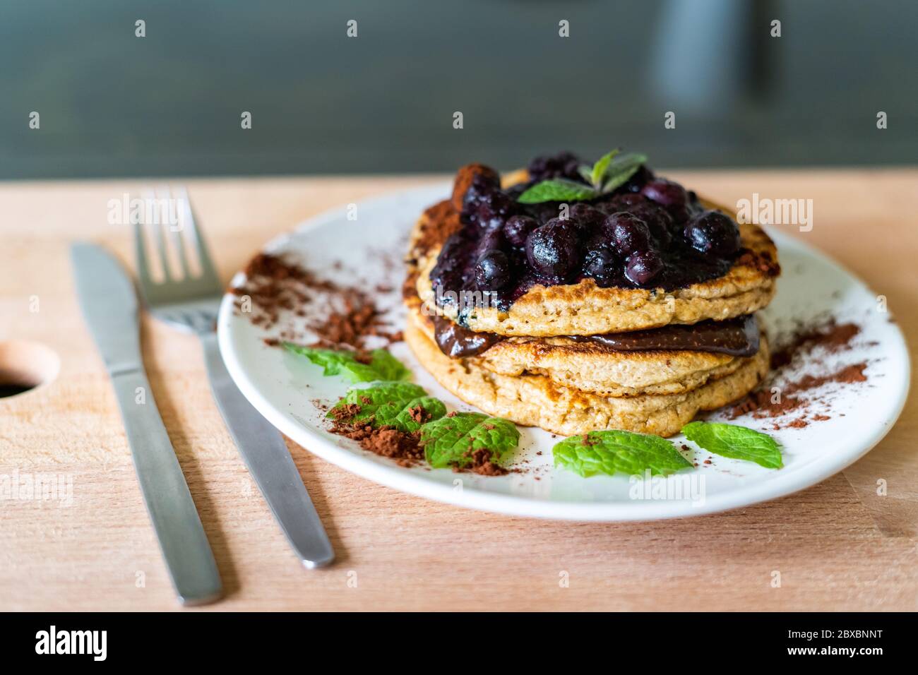 Delicious oats American pancakes with homemade chocolate toping, cooked blueberries and fresh mint leafs. Healthy lifestyle cooking Stock Photo