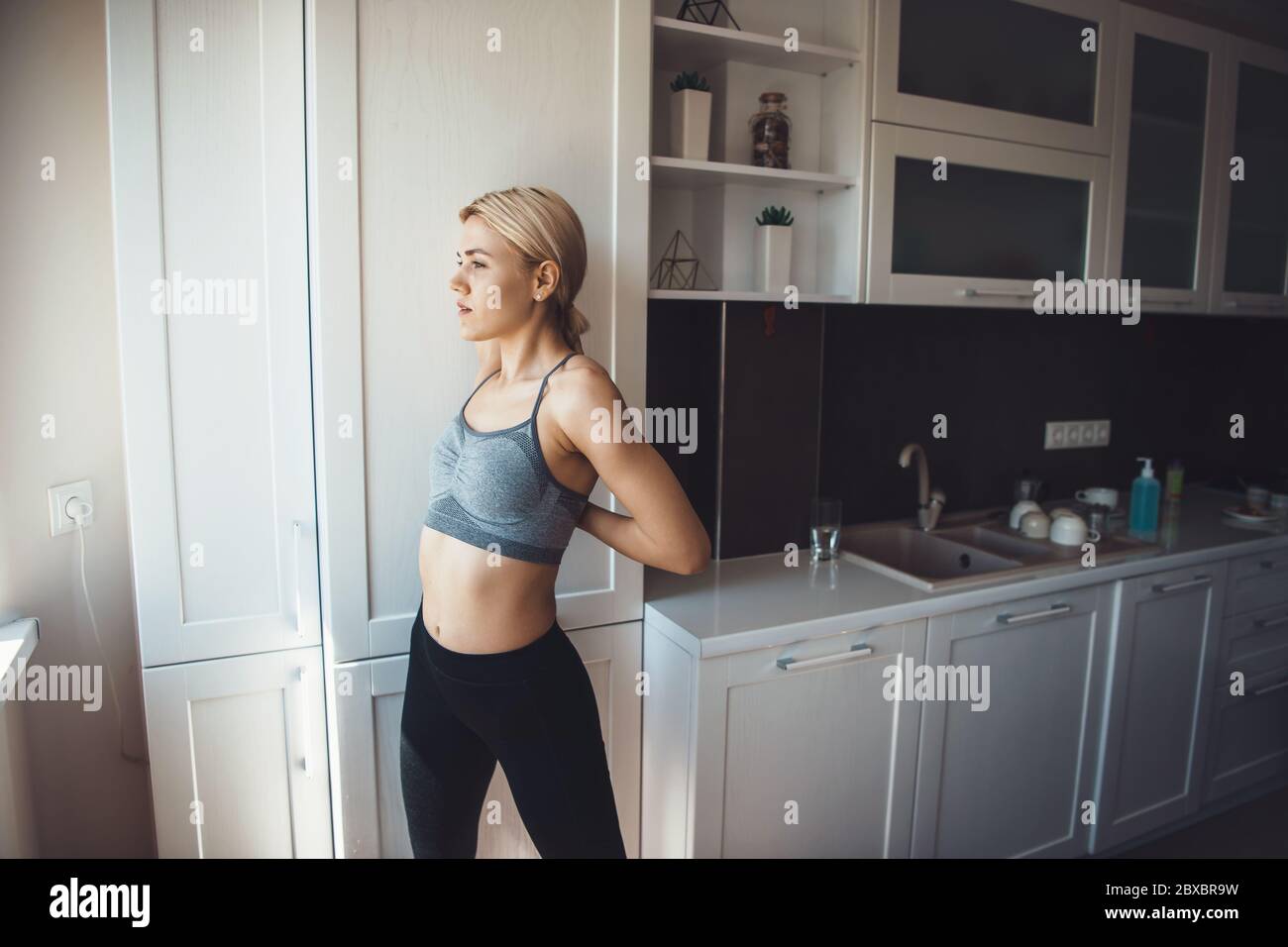Caucasian girl dressed in activewear is stretching her backbone before doing fitness at home Stock Photo