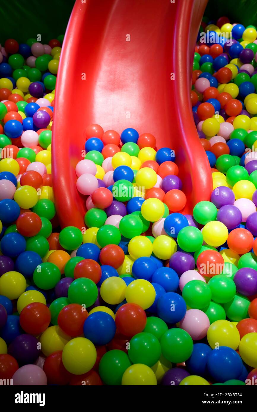 Close up of childrens ball pit or ball pool and a red slide with no people.  The pit is filled with plastic balls and is a playground for children Stock  Photo -