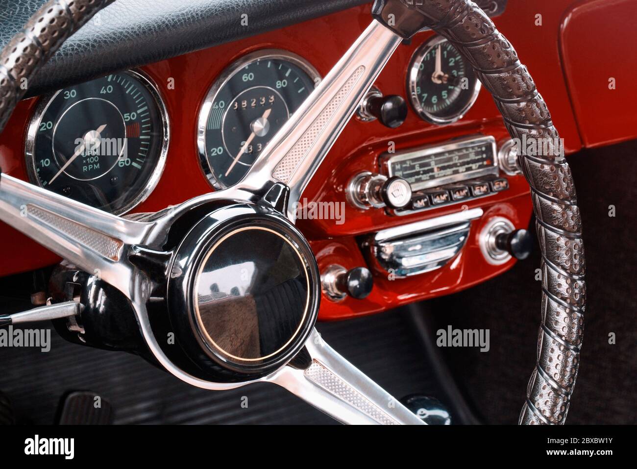 Steering wheel, speedometer, revs, clock dials, radio scale, buttons and knobs on front panel red coupe old timer sports car Stock Photo