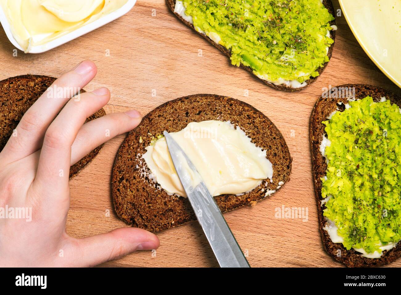 A girl prepares an avocado sandwich. A close-up hand holds bread and spreads cheese. Ready-made sandwiches on a wooden Board. Stock Photo