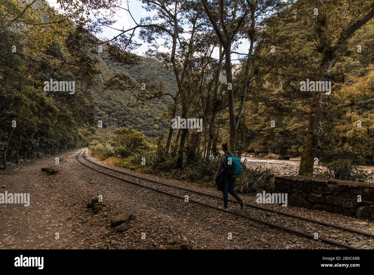 Blonde backpacker woman hiking by a railroad besides a river in the middle of the forest Stock Photo