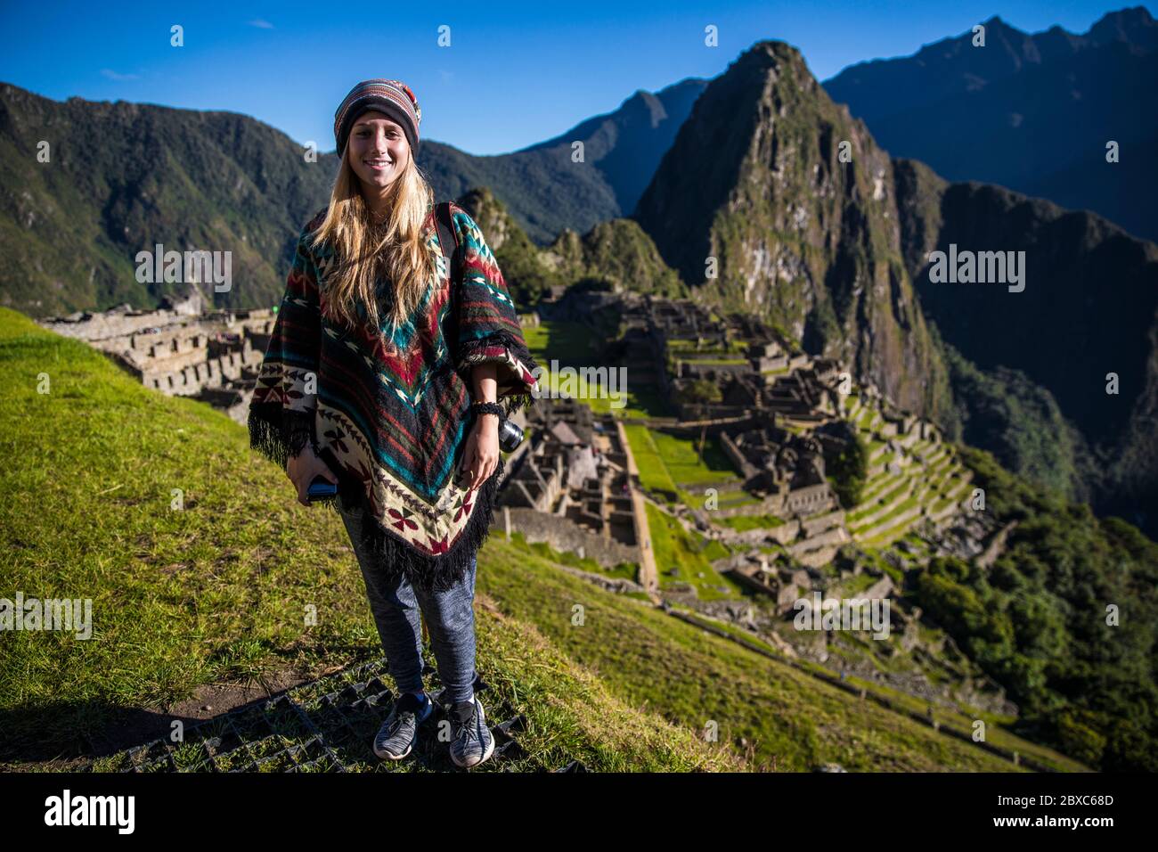 Blonde woman standing on a mountain in Machu picchu smiling at the camera Stock Photo