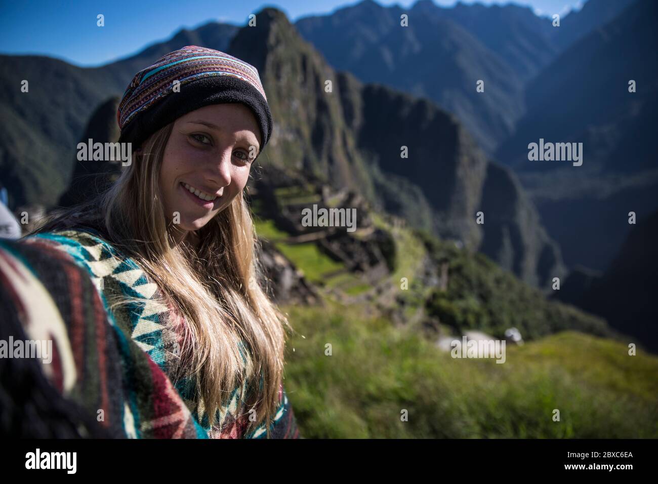 Blonde woman standing on a mountain in Machu picchu smiling at the camera sin a selfie Stock Photo