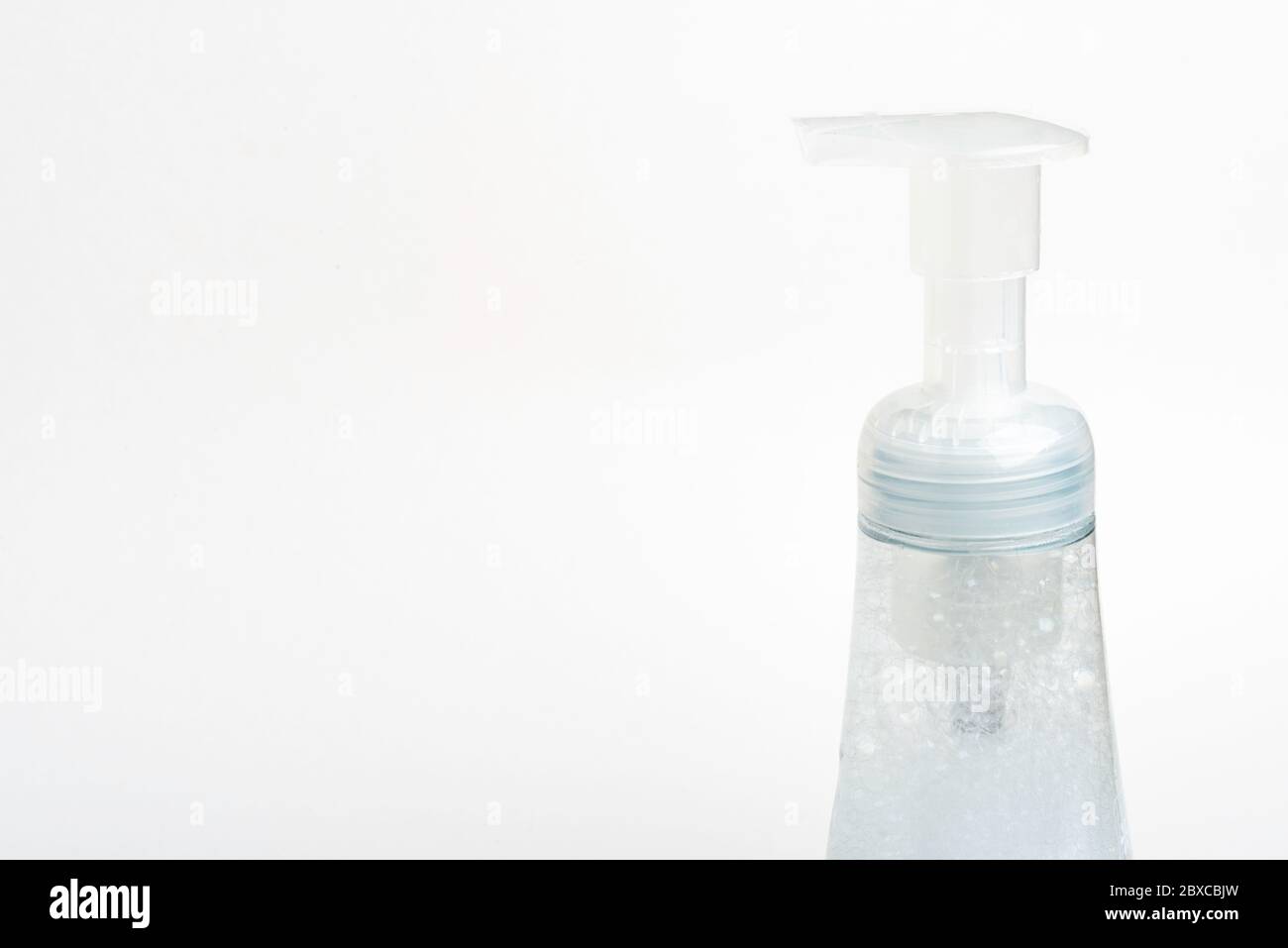 A close-up image of the translucent top pump and bottle of a foam soap plastic dispenser set on a white background. Stock Photo