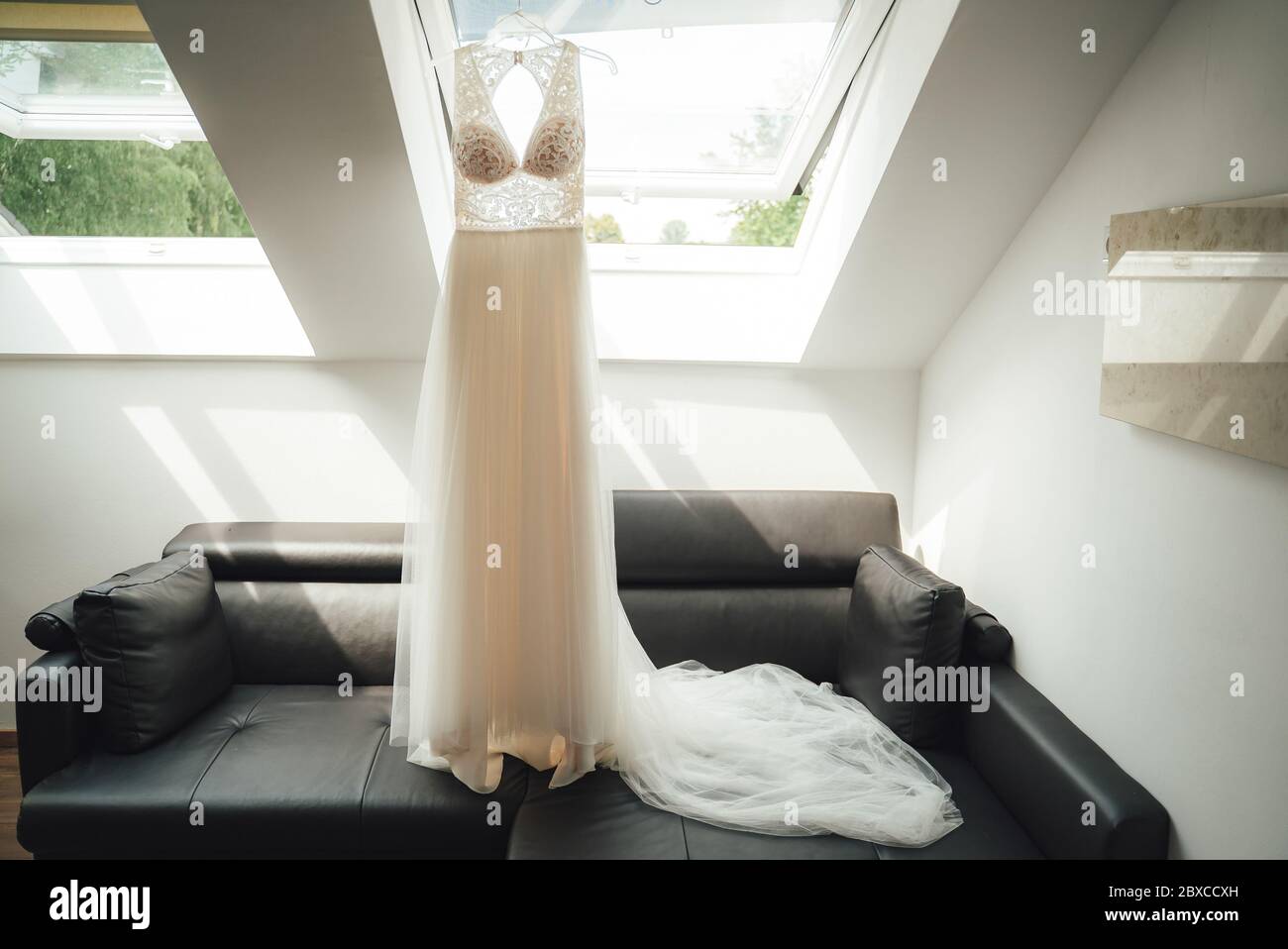 White wedding gown on hanger hanging on roof window frame in attic