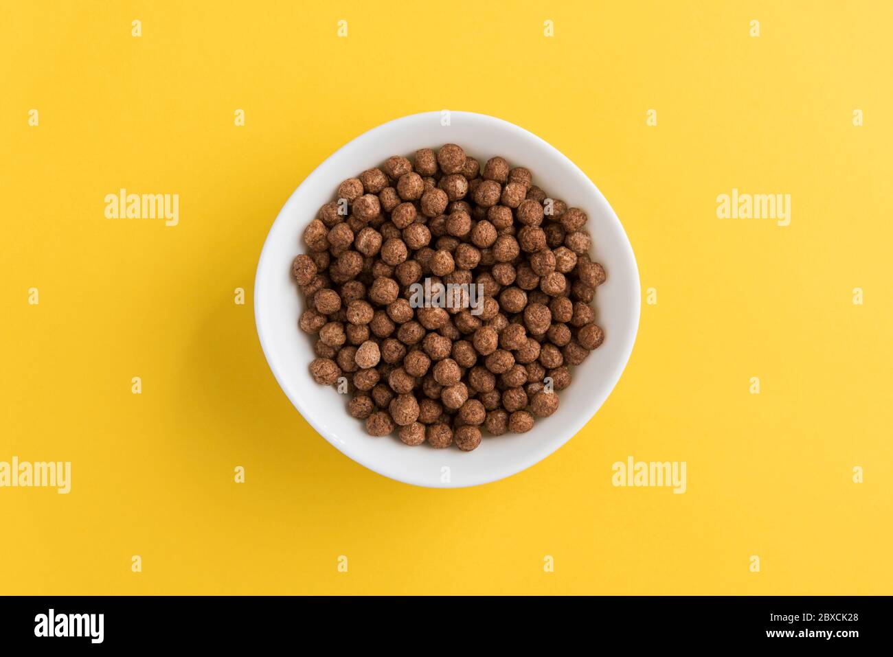 White bowl full of chocolate corn cereal balls on yellow background