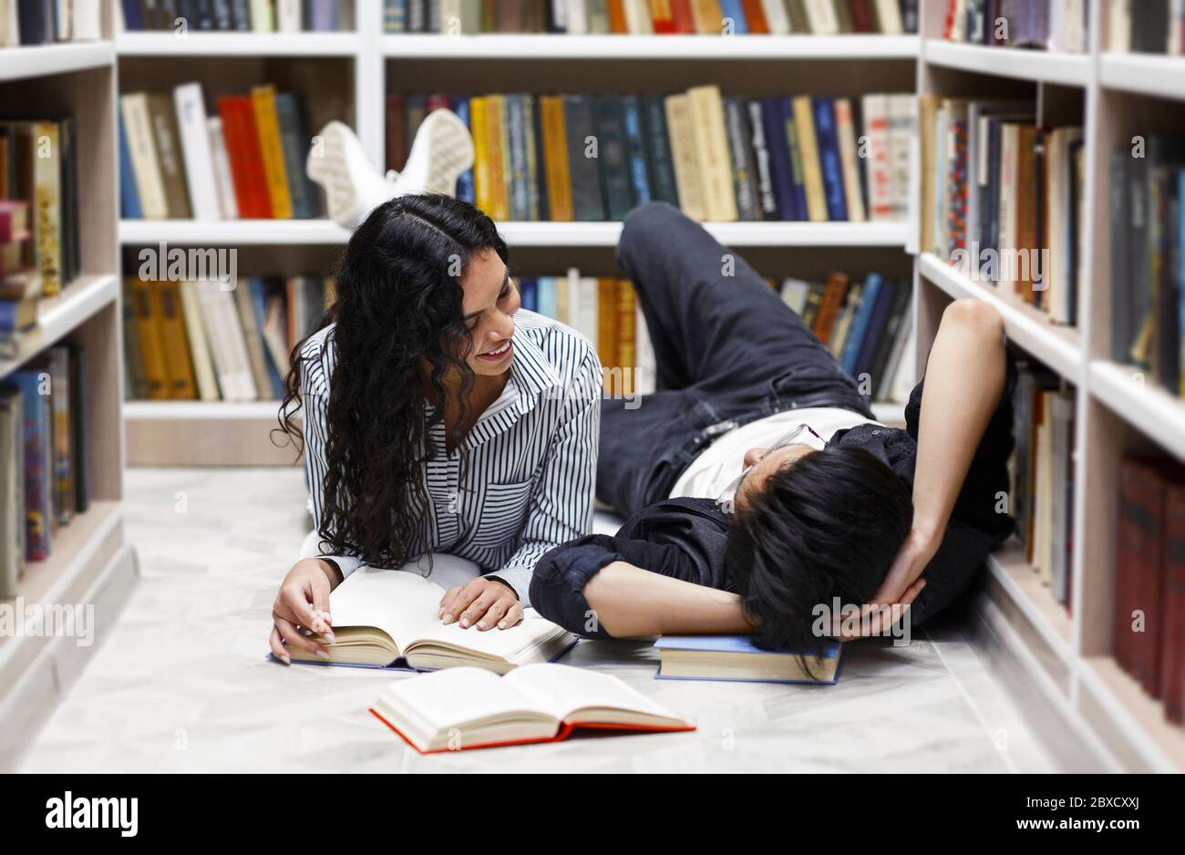 Two multiracial students lying on the floor at library Stock Photo