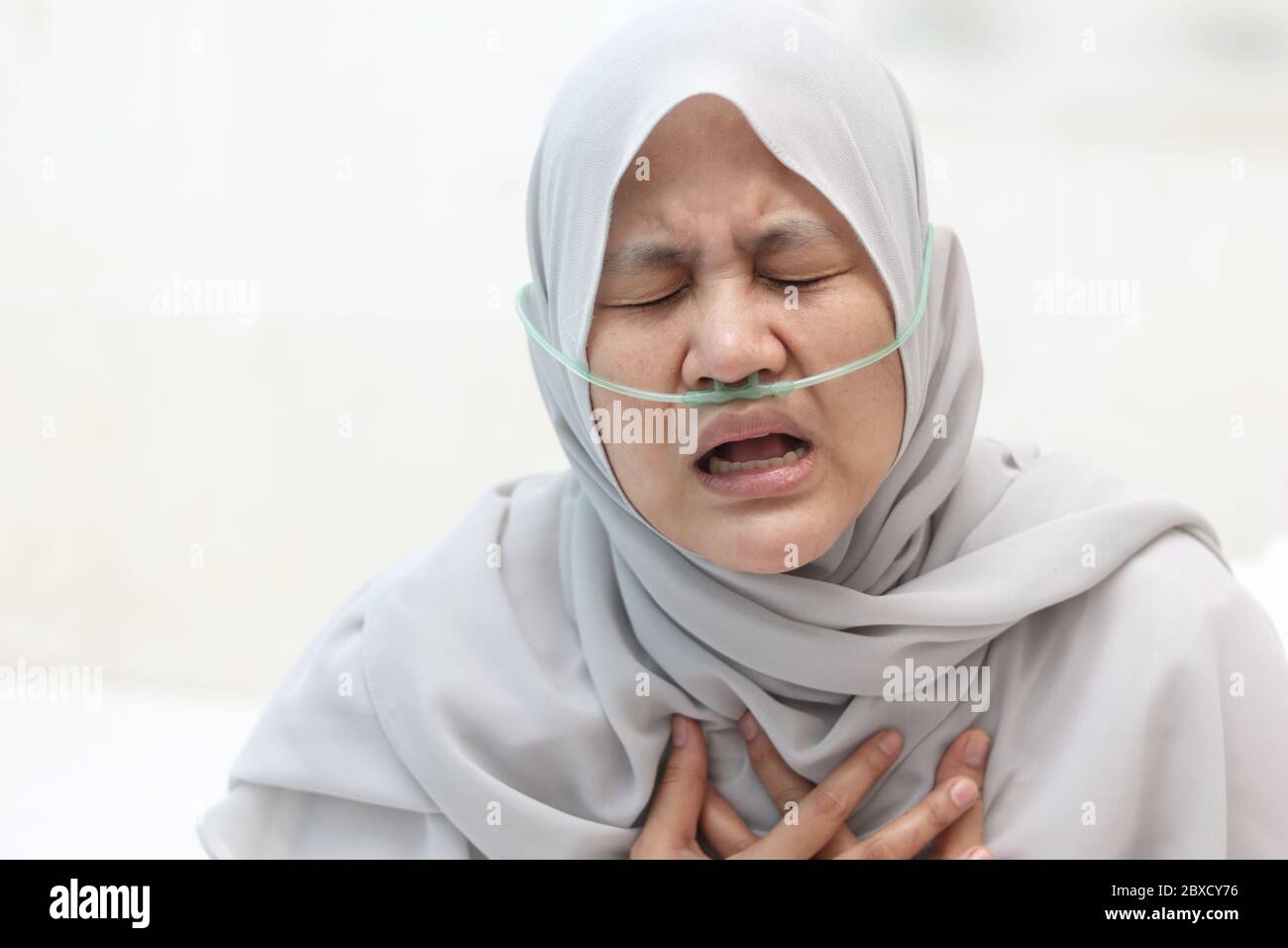 Asian muslim woman having asthma and hard to breathing while her hand touching chest against white background. Covid-19 patient in hospital suffer fro Stock Photo