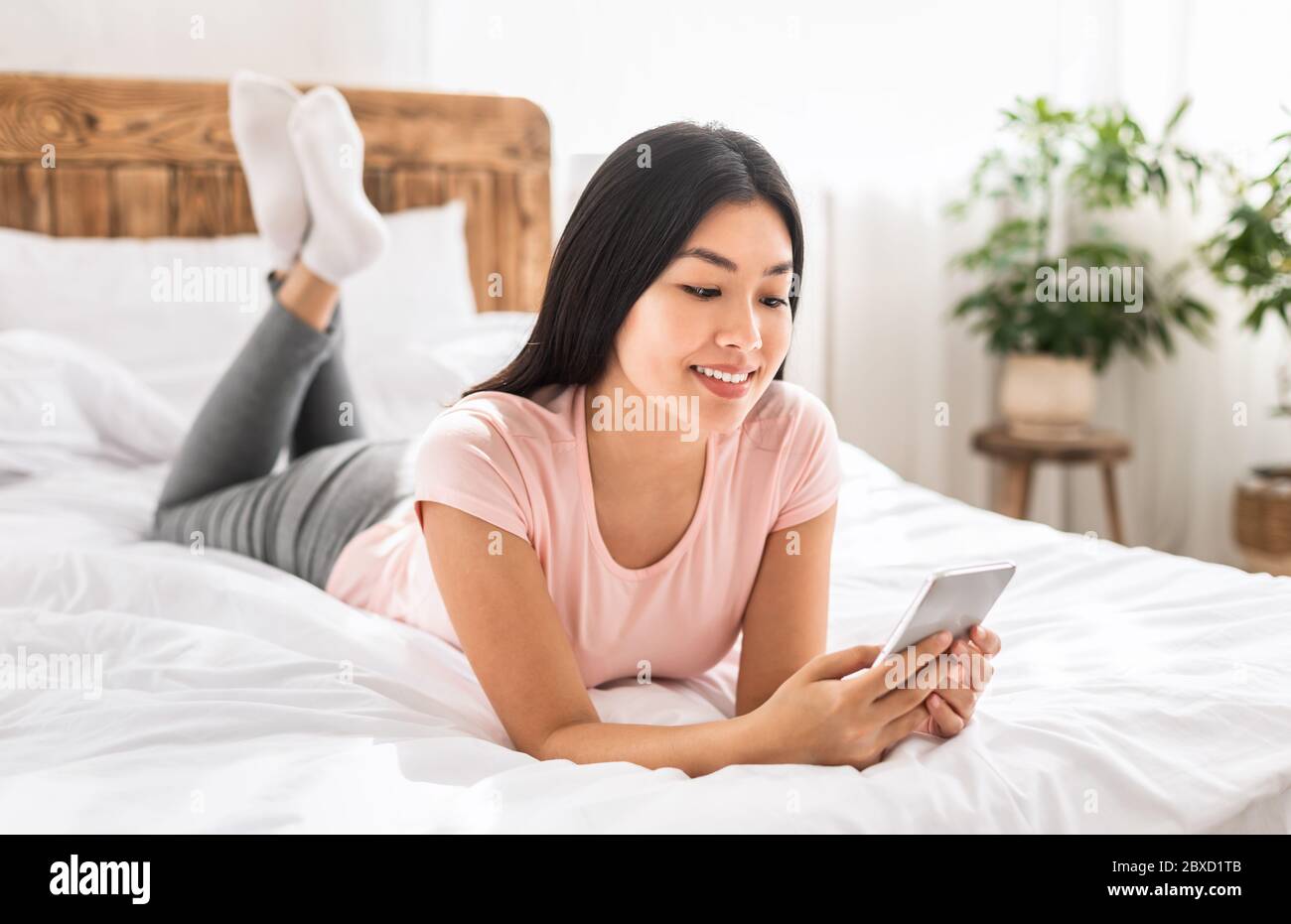 Japanese Girl Using Cellphone Texting With Friends Lying On Bed Stock Photo