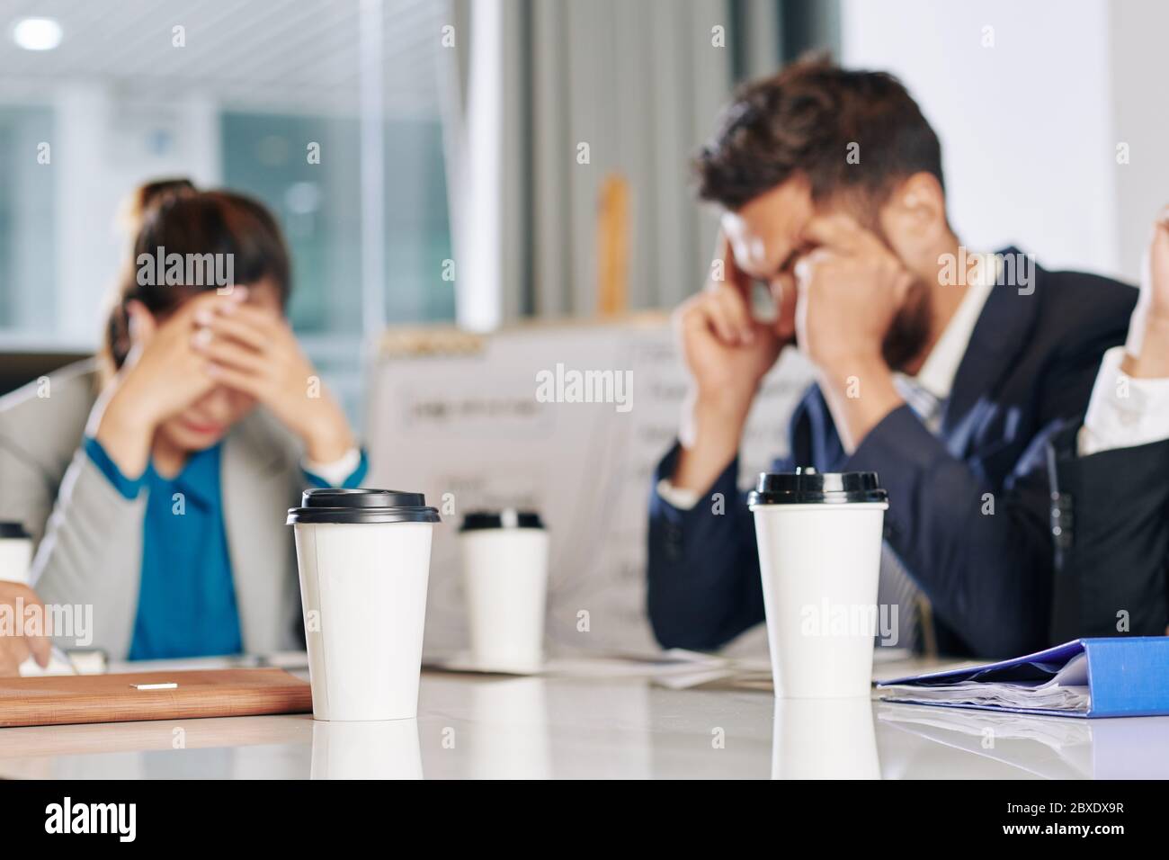 Cups of take out coffee on table in front of business people meeting to discuss economic consequences of covid-19 pandemic Stock Photo