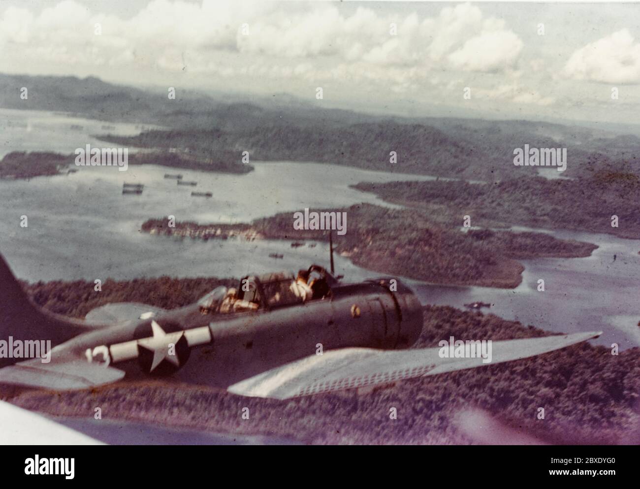 Douglas SBD Aircraft over Segi Point, circa 1943-1944. Segi Point, New Georgia, Solomon Islands. Douglas SBD Aircraft over Segi Point, circa 1943-1944. Note LSTs in harbor below. Stock Photo