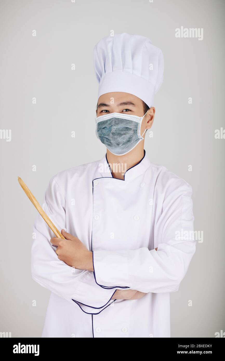 Portrait of positive restaurant chef in medical mask holding wooden spoon Stock Photo